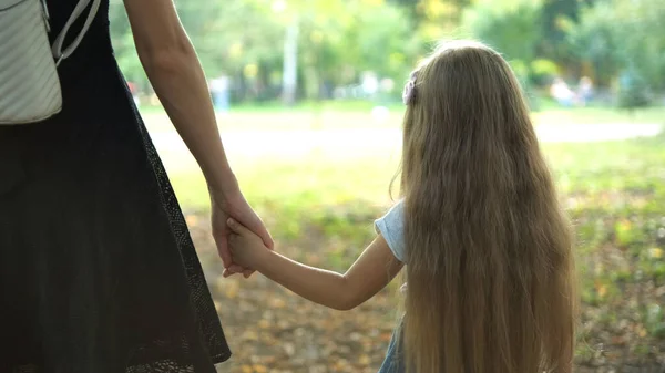 엄마와 작은 딸 이 긴 머리를 하고 여름 공원에서 손을 잡고 걷고 있는 모습 — 스톡 사진