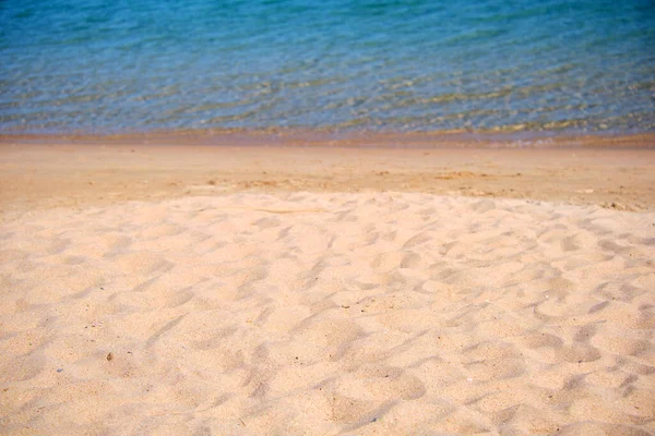 Tengerfenék kék tengervíz felszínével, kis hullámokkal a sárga homokos strandon. Utazási és nyaralási koncepció — Stock Fotó