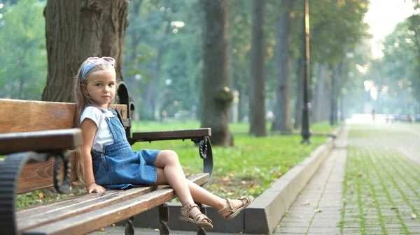 Klein gelukkig kind meisje zitten op een bank rusten in de zomer park — Stockfoto