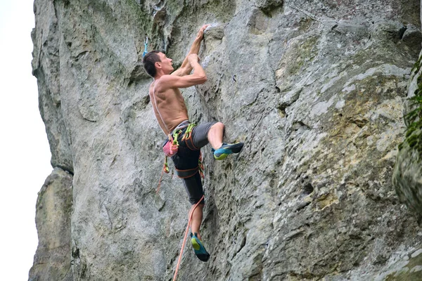 Silny mężczyzna wspinaczka stroma ściana skalistej góry. Sportowiec pokonuje trudną trasę. Zaangażowanie się w ekstremalne hobby sportowe — Zdjęcie stockowe