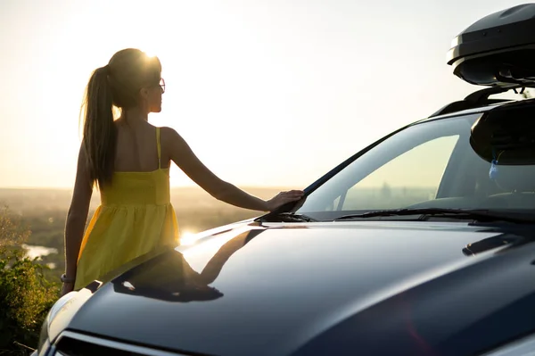 Yong feliz conductor femenino descansando cerca de su coche disfrutando de la vista de la puesta del sol de la naturaleza de verano. Concepto de viaje y recreación — Foto de Stock