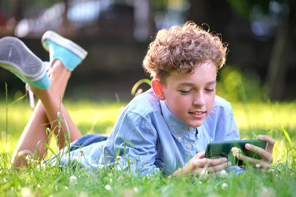 Niño jugando juego en su teléfono inteligente al aire libre en el parque de verano. Adicción desde el concepto de aparatos electrónicos — Foto de Stock