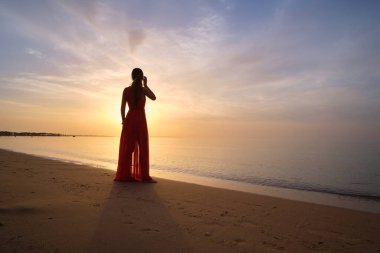 Genç bir kadın okyanus kumsalında tek başına sıcak tropikal bir akşamın tadını çıkarıyor.