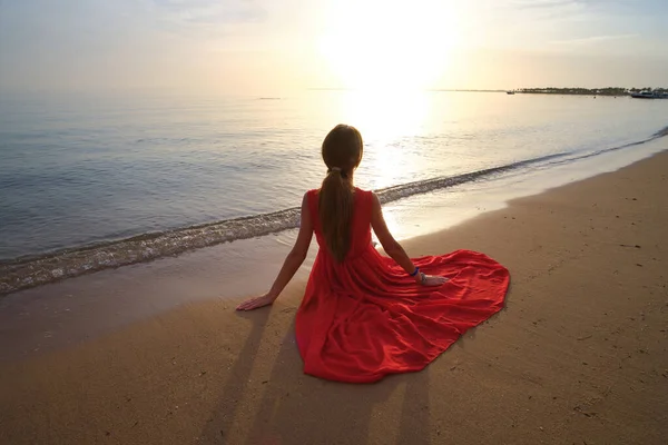 Giovane donna felice in abito rosso rilassante sulla spiaggia di sabbia dal mare godendo calda mattina tropicale — Foto Stock