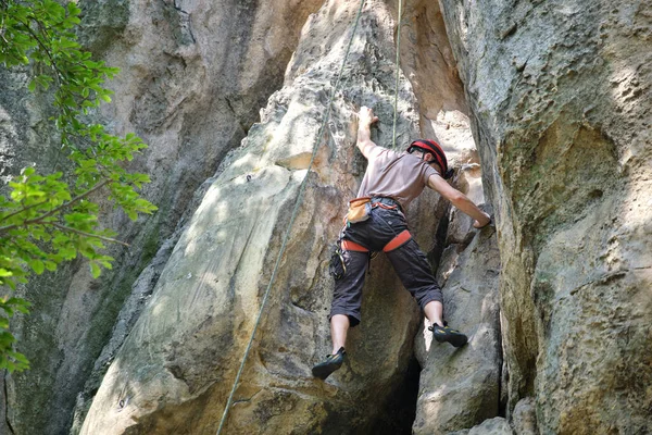 Junger Mann klettert steile Felswand hinauf. Männlicher Bergsteiger bewältigt anspruchsvolle Route Engagement im Extremsportkonzept — Stockfoto