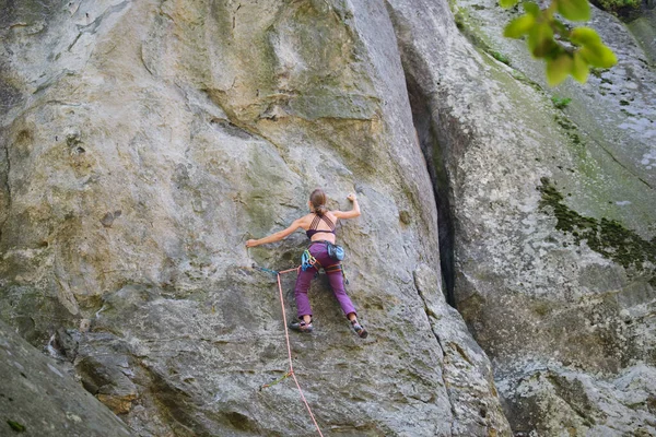 若い女性岩の山の急な壁を登る。登山家は困難な道を克服します。極端なスポーツの概念に従事 — ストック写真