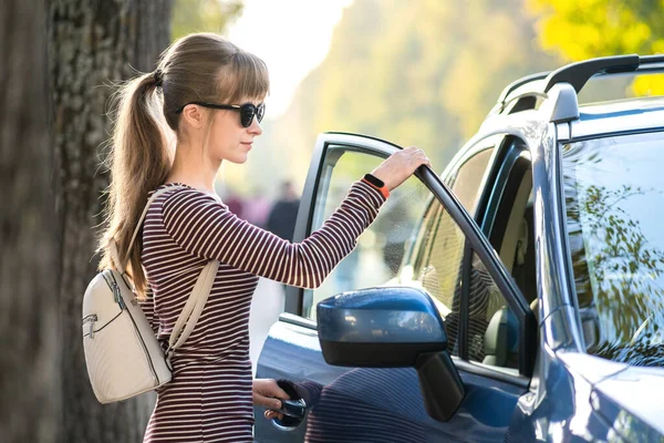 Молодая женщина-водитель наслаждается теплым летним днем, стоя рядом со своей машиной на городской улице. Концепция путешествий и отдыха — стоковое фото