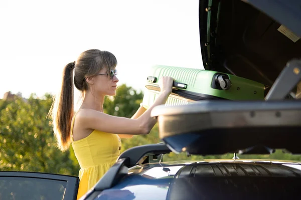 Conductora joven tomando la maleta verde del portaequipajes del coche. Concepto de viajes y vacaciones — Foto de Stock