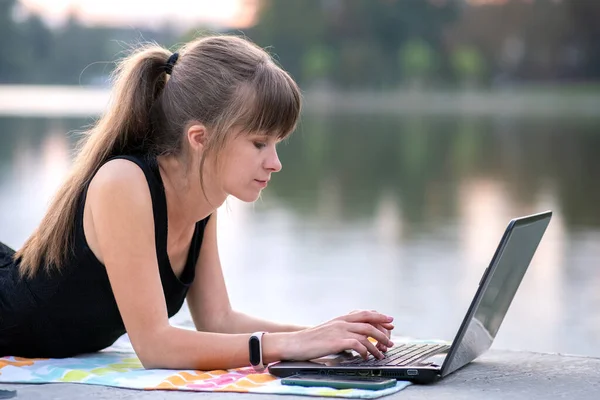 Mujer joven que trabaja detrás de la computadora portátil acostado en el parque de verano al aire libre — Foto de Stock