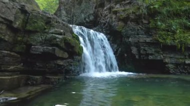 Yazın yağmur ormanlarında kayalık kayalıklardan dökülen beyaz köpüklü suyla dağ nehrindeki muhteşem şelale manzarası.
