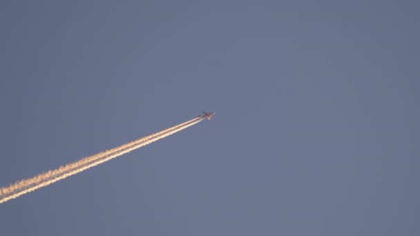 Avionul de pasageri îndepărtat care zboară la mare altitudine pe cerul albastru, lăsând urme de fum alb de contrail în urmă. Conceptul de transport aerian — Videoclip de stoc