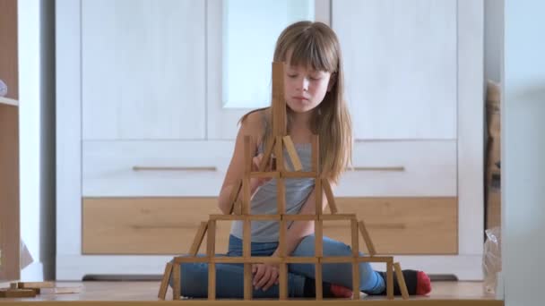 Счастливая девочка играет в игру, складывая деревянные игрушечные блоки в высокой свайной конструкции. Концепция управления движением рук и создания вычислительных навыков — стоковое видео