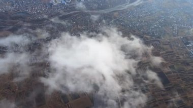Yağmurdan önce oluşan kabarık kümülüs bulutlarıyla kaplı uzak şehrin yüksek irtifasından hava manzarası. Bulutlu manzaraya uçak bakışı