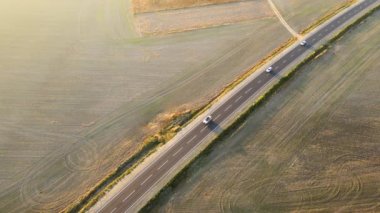 Gün batımında hızlı giden arabalarla şehirlerarası yol manzarası. Akşamları otoban trafiğinin insansız hava aracı görüntüsü