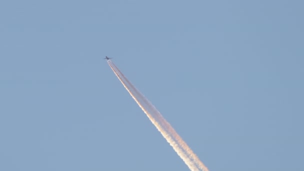 Distant passenger jet plane flying on high altitude on clear blue sky leaving white smoke trace of contrail behind. Air transportation concept — Stock Video