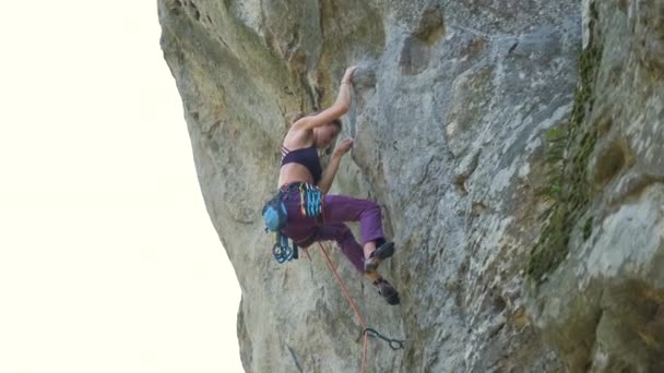 Молода жінка піднімається крутою стіною скелястої гори. Дівчина скелелазіння долає складний маршрут. Залучення до екстремальної спортивної концепції — стокове відео
