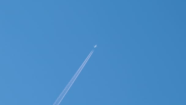 Avião de passageiros distantes voando em alta altitude no céu azul claro deixando vestígios de fumaça branca de contrail para trás. Conceito de transporte aéreo — Vídeo de Stock