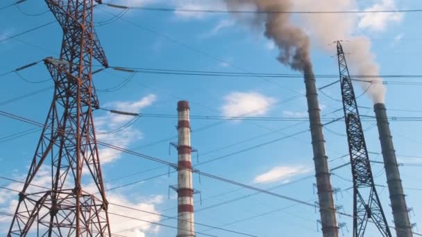 Wysokonapięciowe słupy elektryczne przeciwko wysokonapięciowej elektrowni węglowej wysokie rury z czarnym dymem poruszającym się w górę zanieczyszczającą atmosferę. Produkcja energii elektrycznej z zastosowaniem koncepcji paliw kopalnych — Wideo stockowe