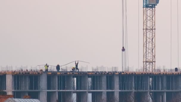 Silhouette sombre de grue à tour et petites silhouettes de travailleurs sur le chantier de construction d'immeubles résidentiels élevés. Développement immobilier — Video