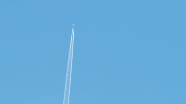Avión a reacción de pasajeros a distancia volando a gran altitud en el cielo azul claro dejando rastro de humo blanco de la estela detrás. Concepto de transporte aéreo — Vídeos de Stock