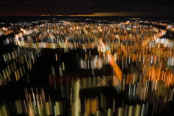 Abstract motion blurred effect of aerial view of buildings and bright illuminated streets in city residential area at night. Dark urban landscape at high altitude — Stock Photo, Image