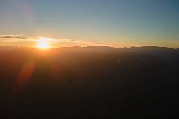 Vista aérea de las oscuras colinas de montaña con brillantes rayos de sol poniente al atardecer. Picos brumosos y valles brumosos por la noche — Foto de Stock