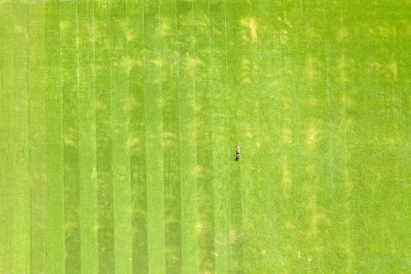 Vista aérea de pequena figura de homem trabalhador aparando grama verde com moagem mashine no campo de estádio de futebol no verão — Fotografia de Stock