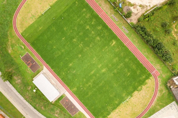 赤のランニングトラックと緑の芝生サッカー場とスポーツスタジアムの空中ビュー — ストック写真