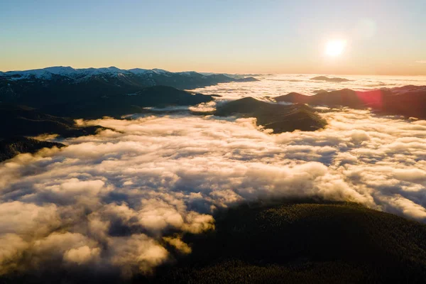 Vzdušný pohled na zářící východ slunce nad bílými hustými mraky se vzdálenými temnými horami na obzoru — Stock fotografie