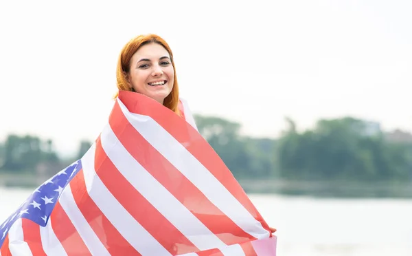 Visão traseira da jovem feliz com a bandeira nacional dos EUA em seus ombros. Menina positiva celebrando o dia da independência dos Estados Unidos — Fotografia de Stock