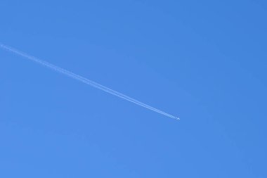 Mesafeli yolcu jet uçağı açık mavi gökyüzünde yüksek irtifada uçarken ardında beyaz duman izi bırakıyor. Hava taşımacılığı kavramı