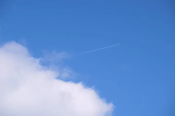 遠くの旅客機は白い雲が後ろの輪郭の煙の跡を残す青い空の高い高度で飛んでいる。航空旅行の概念 — ストック写真