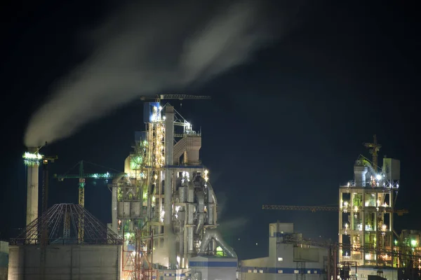 Usine de ciment éclairée avec structure d'usine élevée et grues à tour dans la zone de production industrielle la nuit. Fabrication et concept d'industrie mondiale — Photo