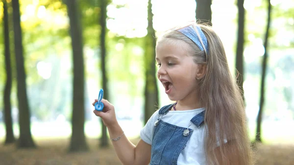 Kleines glückliches Mädchen, das draußen im grünen Park Seifenblasen pustet. Konzept für Sommeraktivitäten im Freien — Stockfoto