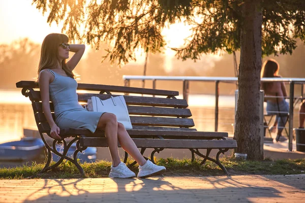 Одинокая женщина, сидящая на скамейке у озера, наслаждается теплым летним вечером. Концепция одиночества и расслабления — стоковое фото