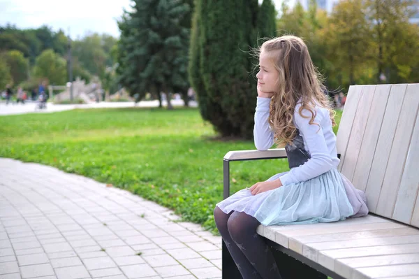 Porträtt av söt barn flicka sitter på parkbänk utomhus — Stockfoto