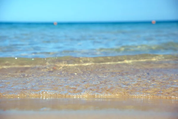 Θαλάσσιο τοπίο με επιφάνεια γαλάζιου θαλασσινού νερού με μικρά κυματιστά κύματα να συντρίβονται σε κίτρινη αμμώδη παραλία. Έννοια ταξιδιού και διακοπών — Φωτογραφία Αρχείου