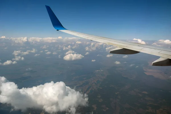 Vista del ala del avión jet desde el interior volando sobre nubes hinchadas blancas en el cielo azul. Concepto de viaje y transporte aéreo — Foto de Stock