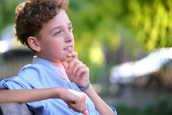 Молодий щасливий хлопчик розслабляється, сидячи на лавці в літньому парку. Позитивна дитина насолоджується літнім часом на відкритому повітрі. Концепція добробуту дітей — стокове фото