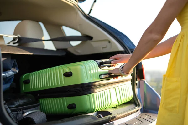 Mujer joven en vestido de verano amarillo tomando maleta verde del maletero del coche. Concepto de viajes y vacaciones — Foto de Stock