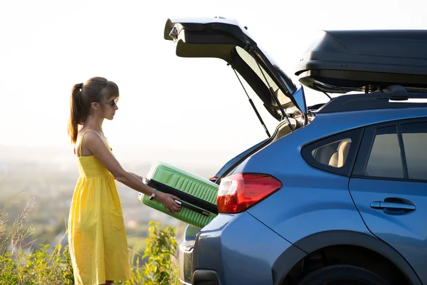 Mujer joven tomando la maleta verde del maletero del coche. Concepto de viajes y vacaciones — Foto de Stock