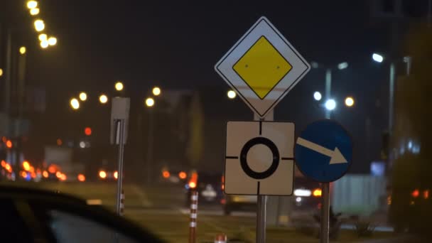 Roundabout road signs with blurred cars on city street traffic at night. Urban transportation concept — Stock Video