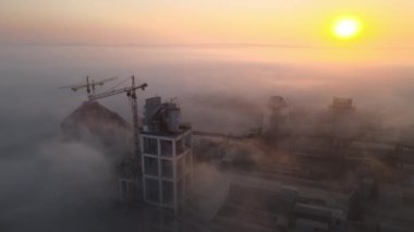 Beton yapılı çimento fabrikasının havadan görünüşü ve sisli bir akşamda endüstriyel üretim alanında kule vinci. Üretim ve küresel sanayi kavramı