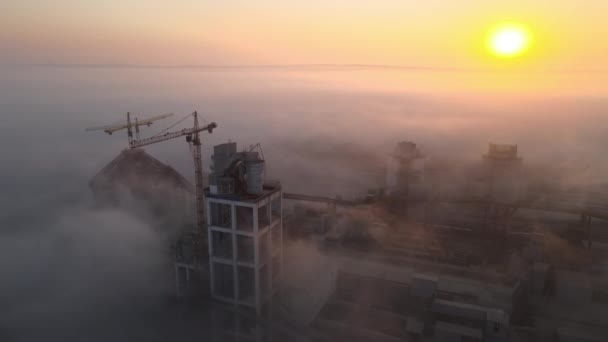 Вид с воздуха на цементный завод с высокой конструкцией бетонного завода и башенный кран на производственной площадке в туманный вечер. Концепция производства и мировой промышленности — стоковое видео