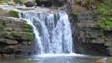 Yazın yağmur ormanlarında kayalık kayalıklardan dökülen beyaz köpüklü suyla dağ nehrindeki muhteşem şelale manzarası.