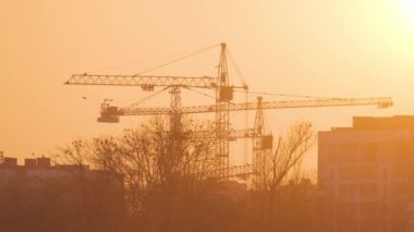 Gün batımında yüksek apartmanlı inşaat alanındaki vinçlerin koyu renkli silueti. Gayrimenkul geliştirme