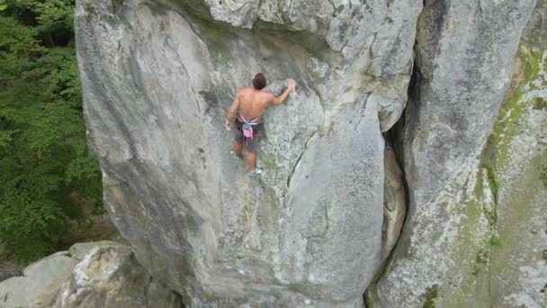 Joven escalando empinada pared de montaña rocosa. Hombre escalador supera ruta desafiante. Participar en el concepto de deporte extremo — Vídeo de stock