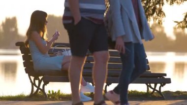 Sıcak bir yaz akşamında, göl kenarındaki bankta tek başına oturan yalnız bir kadın. Yalnızlık ve doğa konseptinde rahatlama.