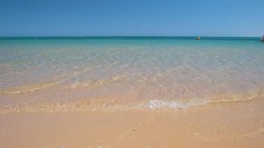 Mavi deniz suyunun yüzeyi ve küçük dalgalı dalgaların sarı kumsala çarptığı deniz burnu. Seyahat ve tatil kavramı