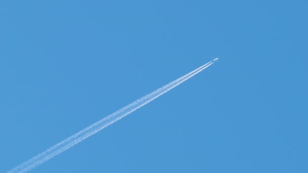 Afstand passagiersvliegtuig vliegen op grote hoogte op heldere blauwe lucht laat witte rook spoor van contrail achter. Luchtvervoersconcept — Stockvideo